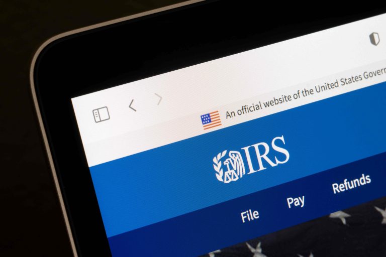 Close-up of a device screen showing the IRS official website header, including the United States government banner, flag icon, and navigation links like File and Pay on a blue background.