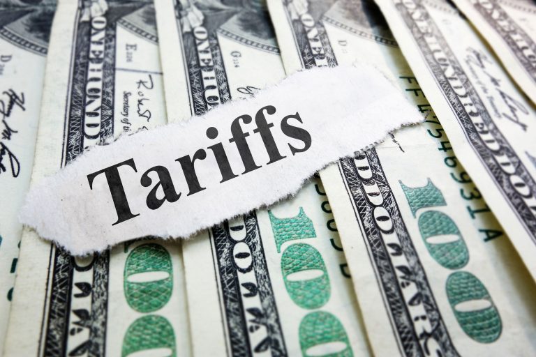 Torn paper strip with the word 'Tariffs' laid over a background of US dollar bills.